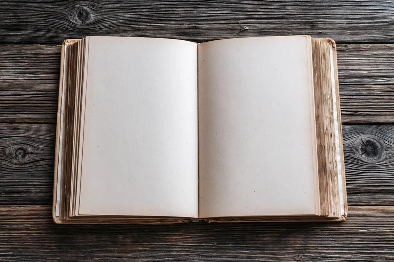 Open hardcover book with blank aged pages lying flat on dark wooden surface