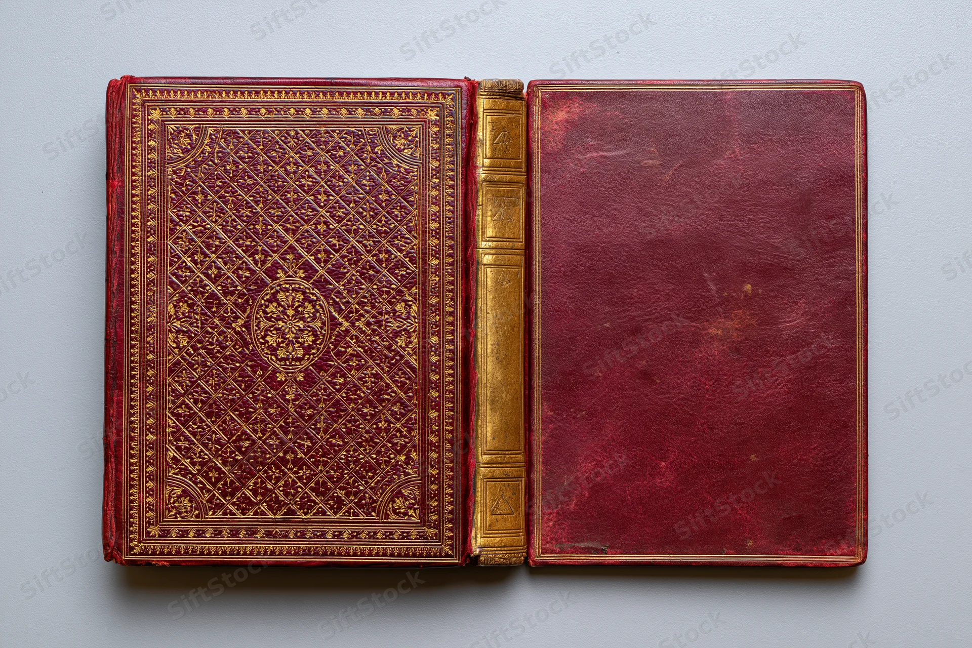 Antique hardcover book open flat showing front and back covers with ornate gold embossing on red leather