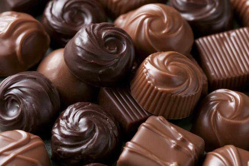 Assorted chocolate pralines and truffles piled closely together in a close-up view