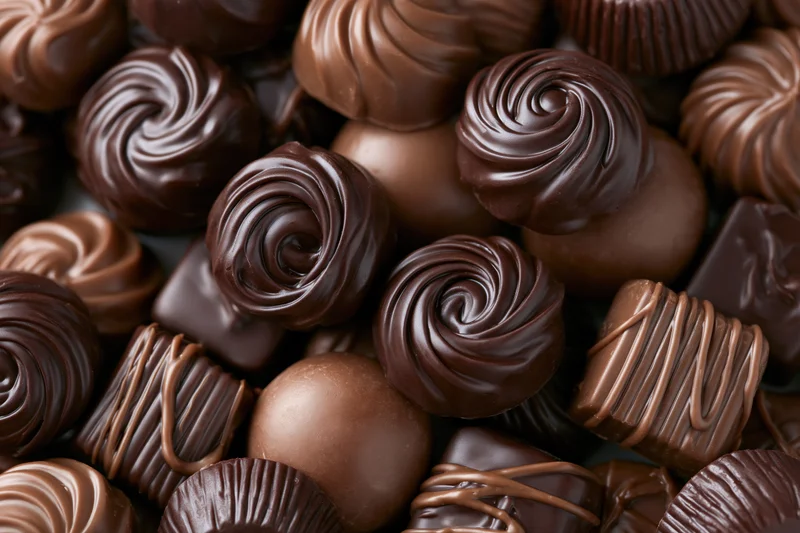 Assorted chocolate pralines and truffles piled closely together in a closeup view