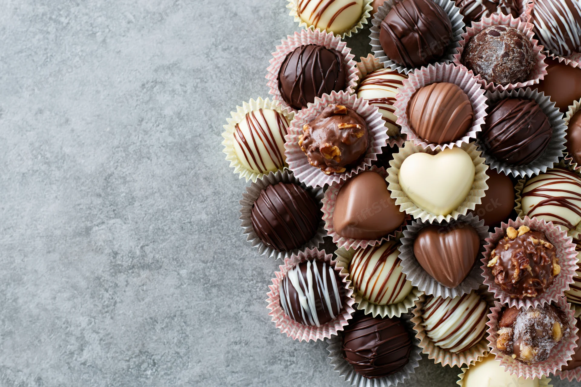 Assorted chocolate truffles and pralines in pastel paper cups arranged on a gray surface with copyspace