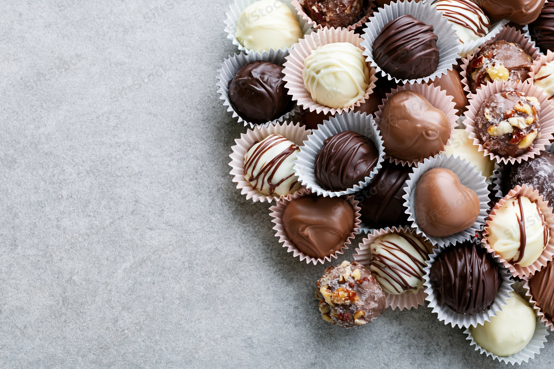 Assorted chocolate truffles and pralines in pastel paper cups arranged on gray surface with copyspace