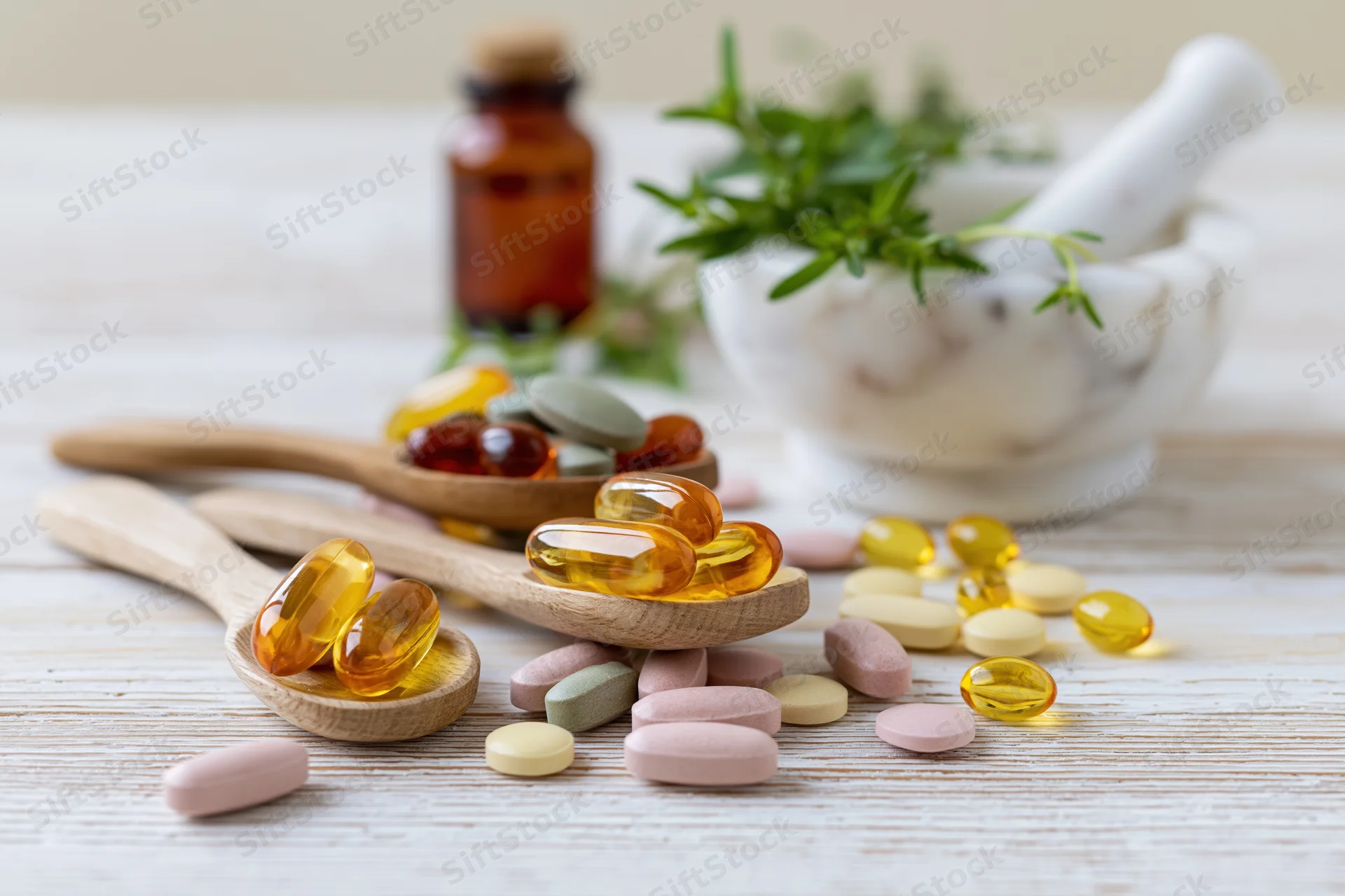 Assorted herbal supplement capsules and fish oil gel caps on wooden spoons with mortar and pestle in background