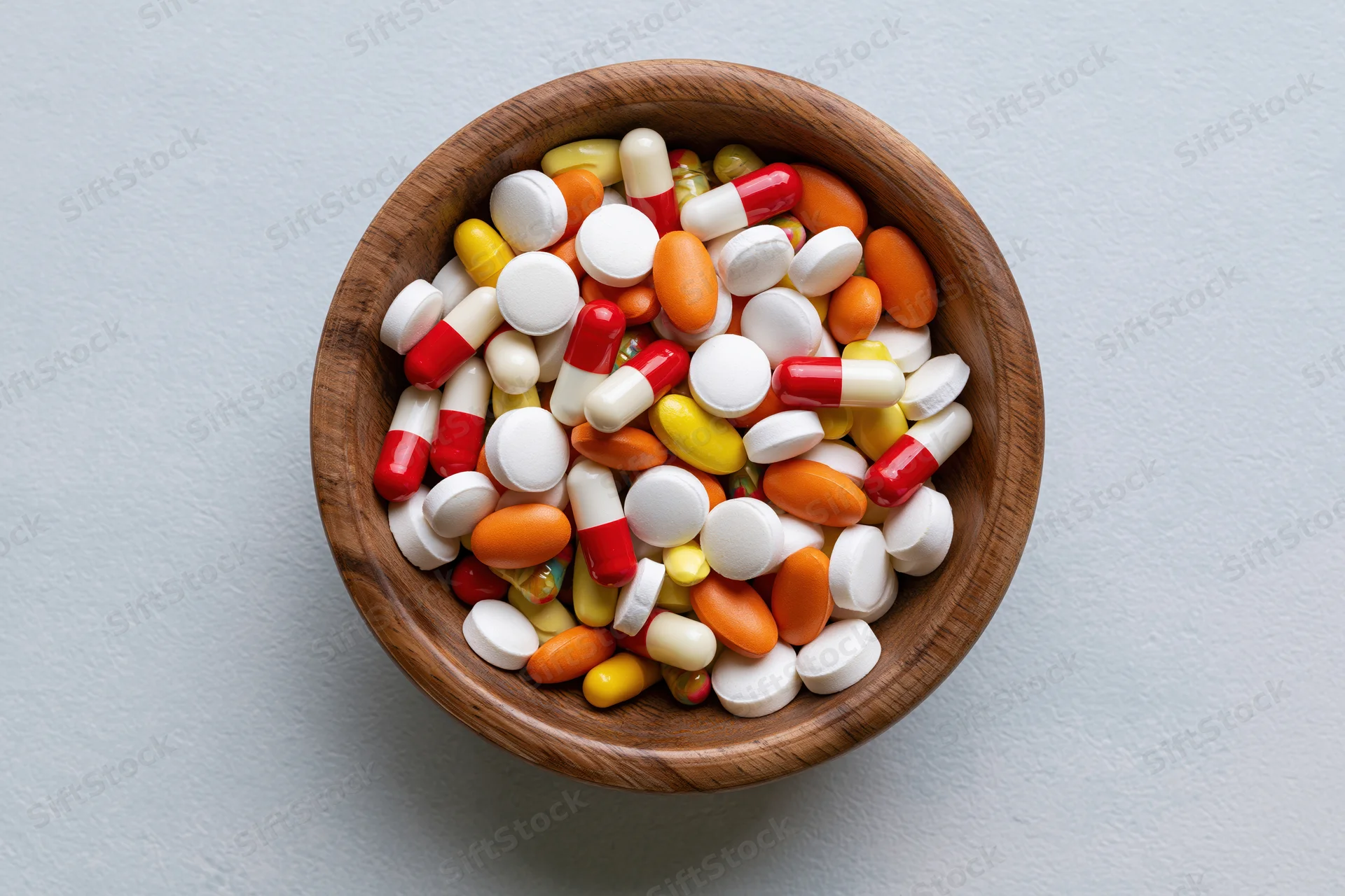 Assorted pharmaceutical pills and capsules in a wooden bowl on a gray surface