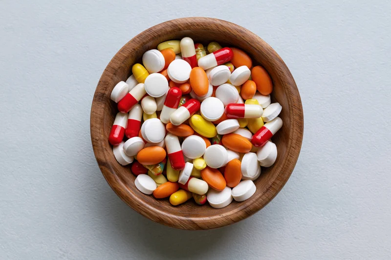 Assorted pharmaceutical pills and capsules in a wooden bowl on a gray surface