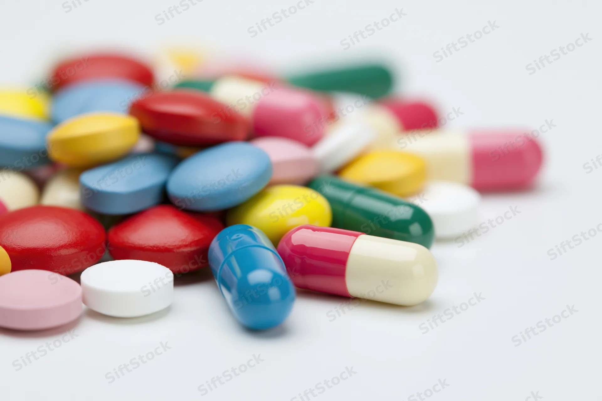 Assorted pharmaceutical pills and capsules scattered loosely on a white surface