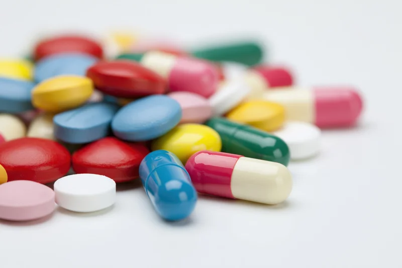 Assorted pharmaceutical pills and capsules scattered loosely on a white surface