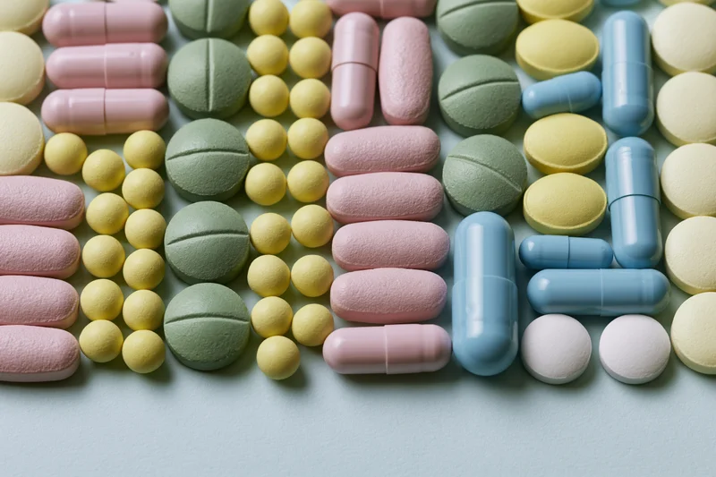 Assorted prescription pills and capsules arranged in loose rows on a light surface