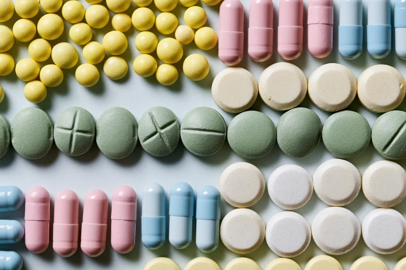 Assorted prescription pills and capsules arranged in loose rows on a light surface