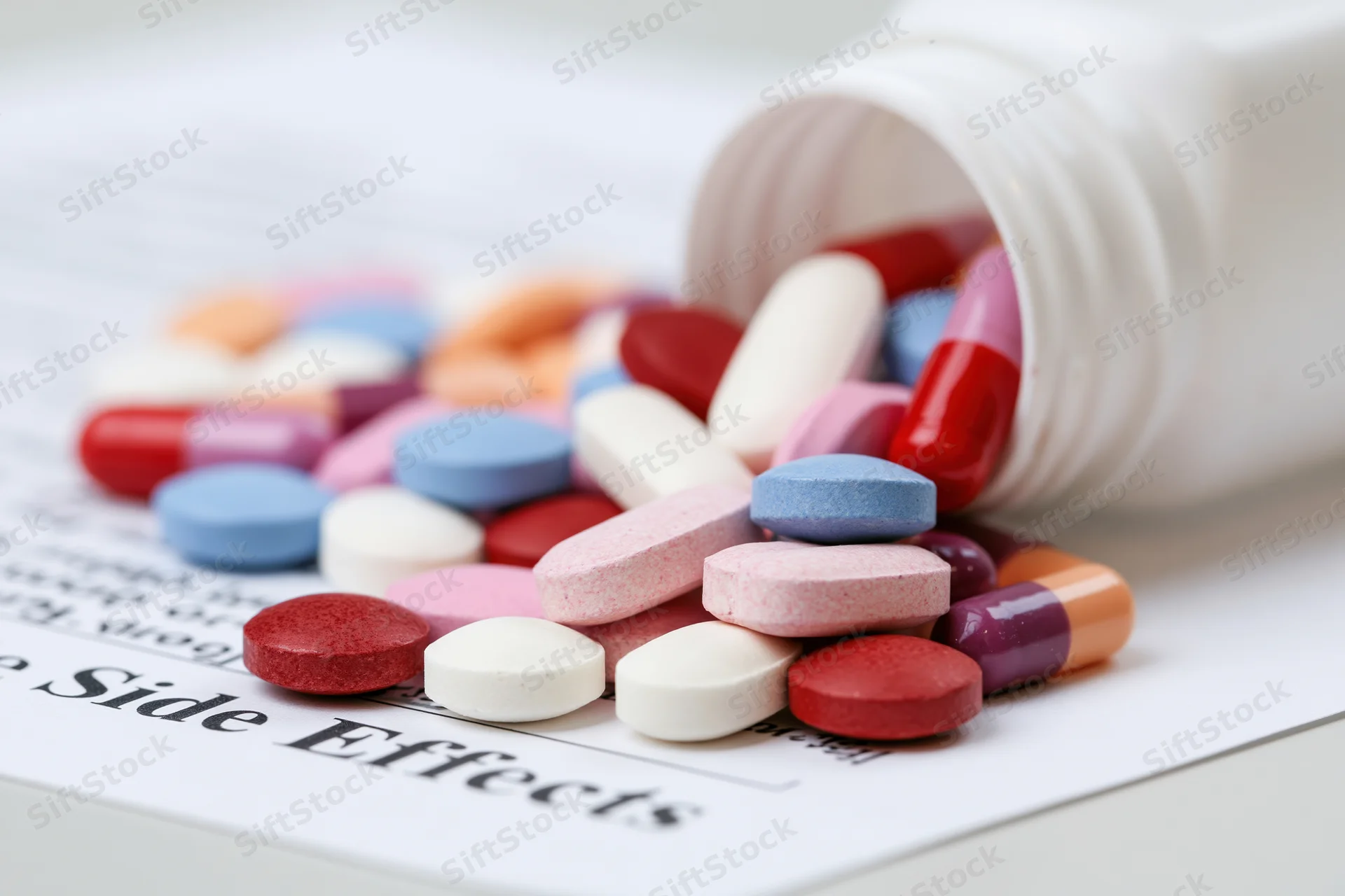 Assorted prescription pills and capsules spilling from a bottle onto a document labeled side effects