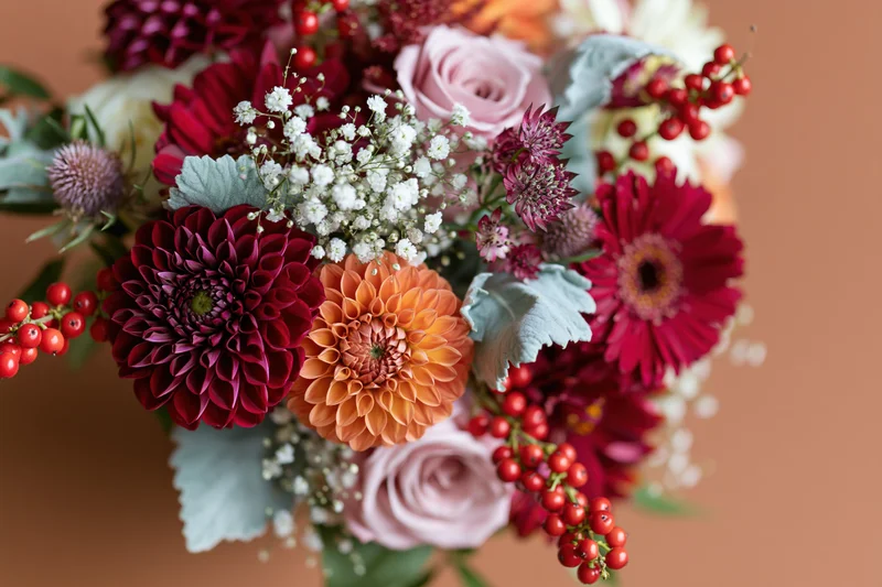 Autumn floral bouquet with dahlias, roses, and red berries arranged in a vibrant composition on a warm background