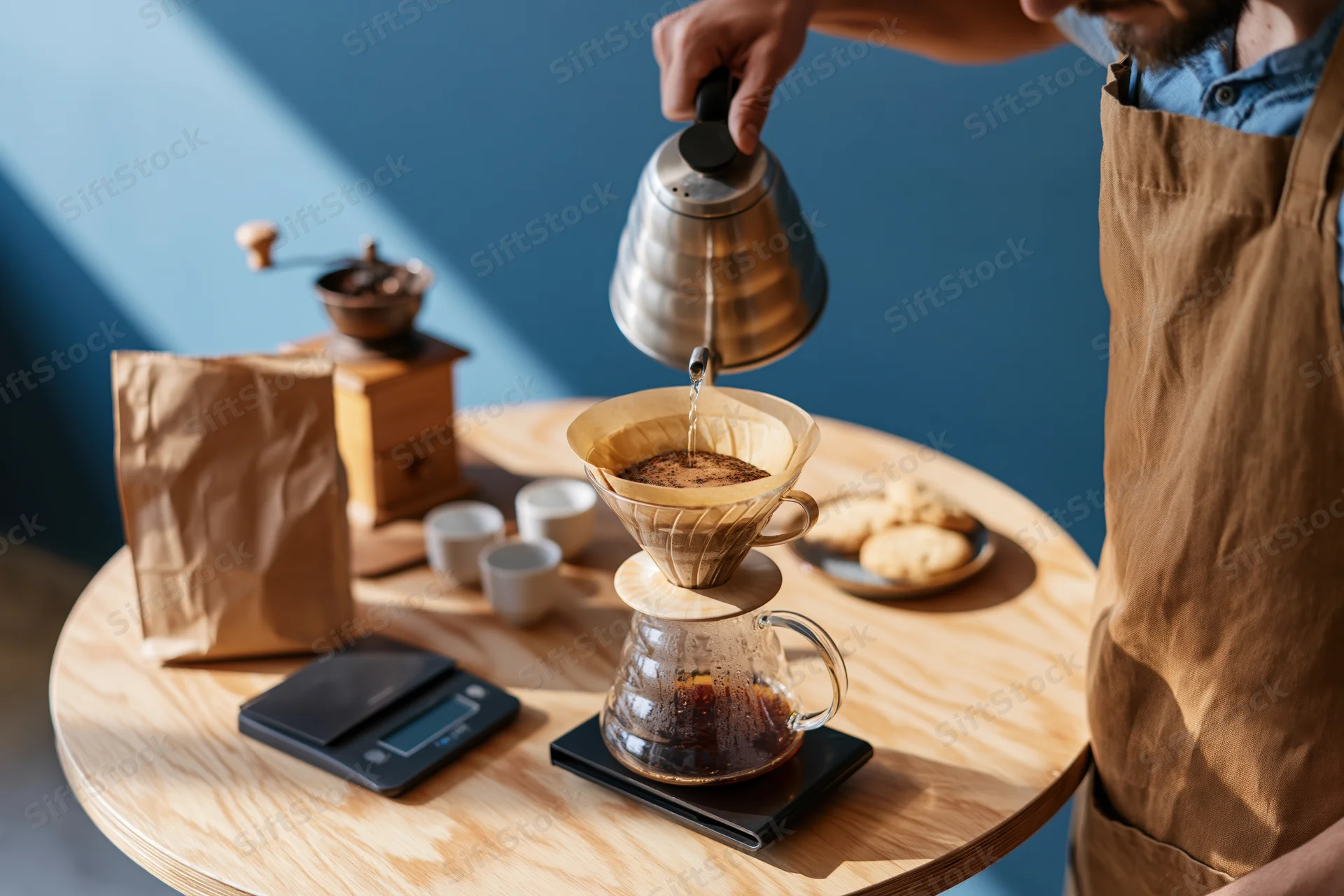 Barista pouring hot water from a gooseneck kettle into a paper filter over a glass carafe on a wooden table