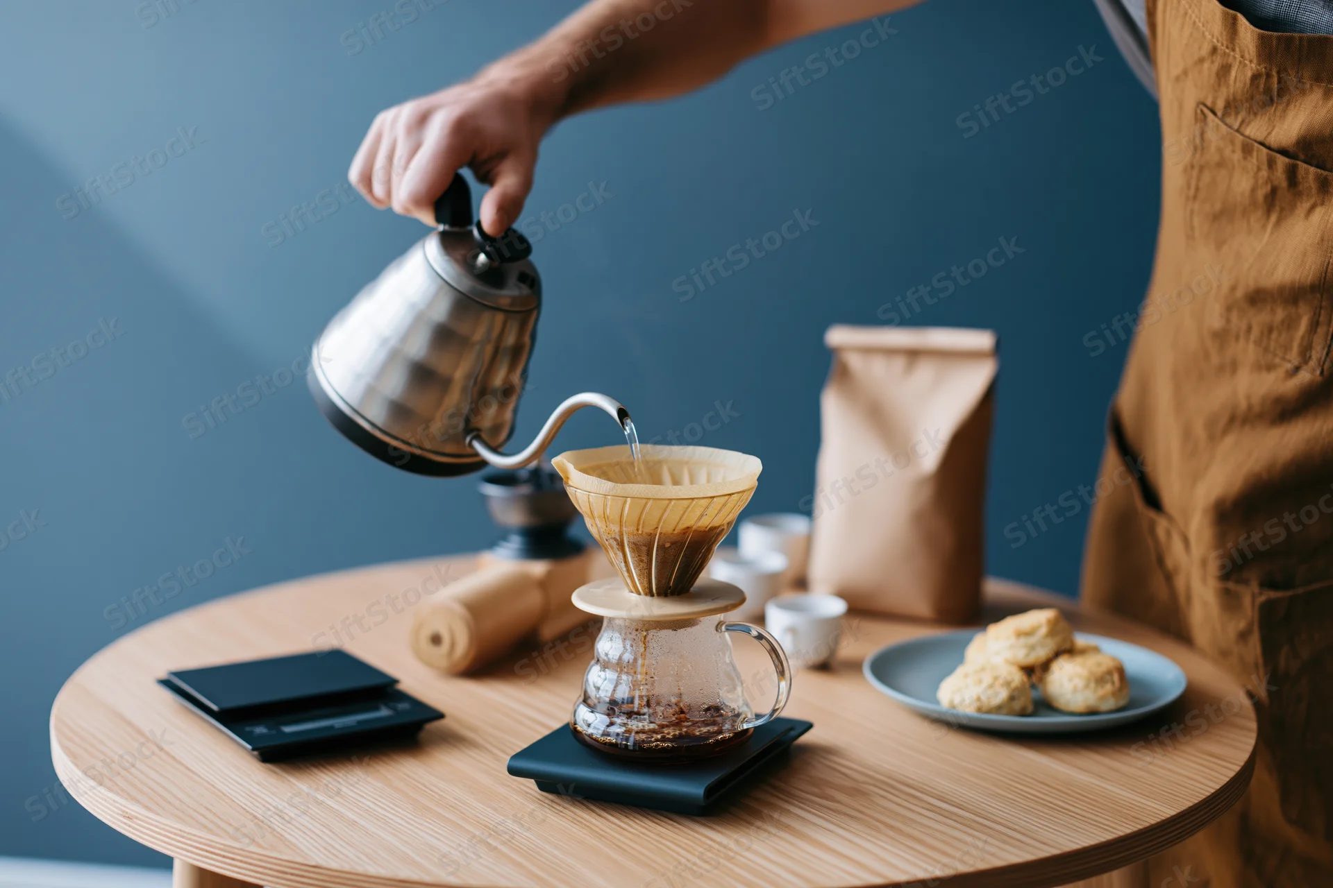 Barista pouring hot water from a gooseneck kettle into a paper filter over a glass carafe on a wooden table