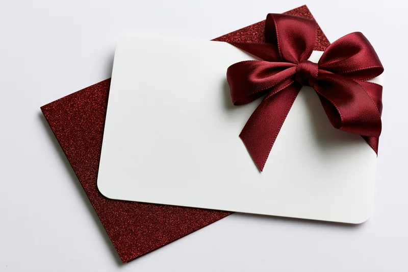 Blank white gift card with red ribbon bow on glitter envelope against white background