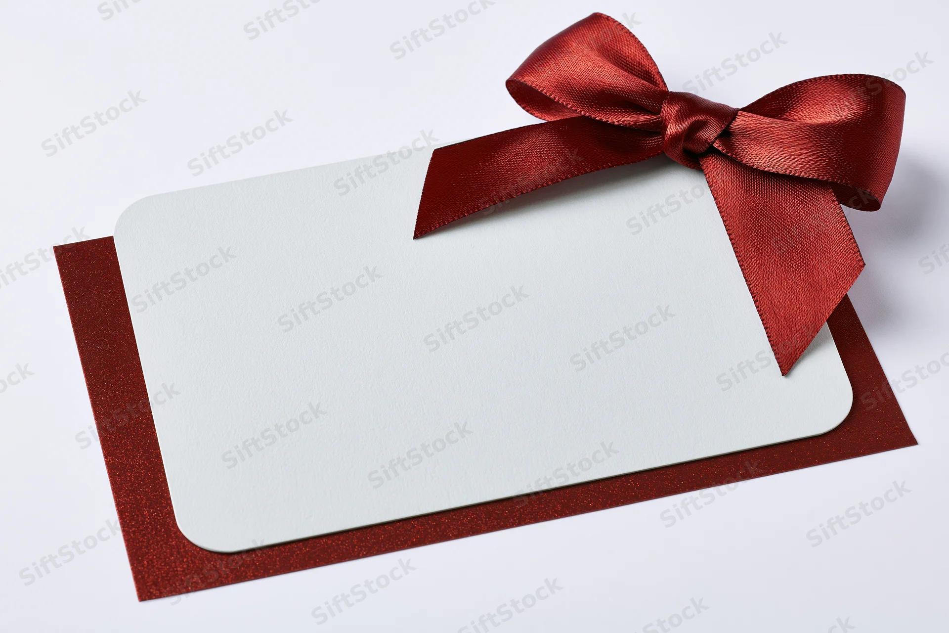 Blank white gift card with red ribbon bow on glittery red envelope against white background