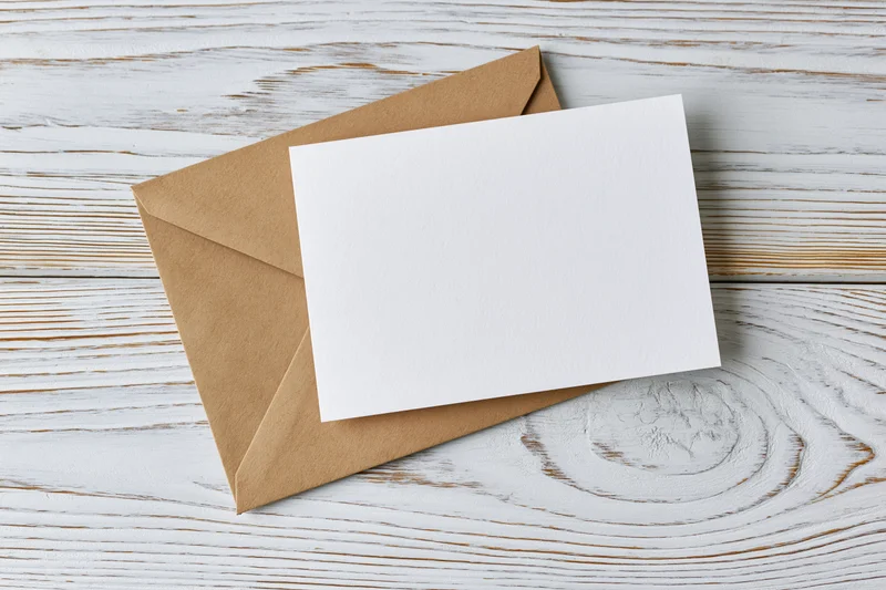 Blank white greeting card resting on a kraft paper envelope on a whitewashed wooden surface