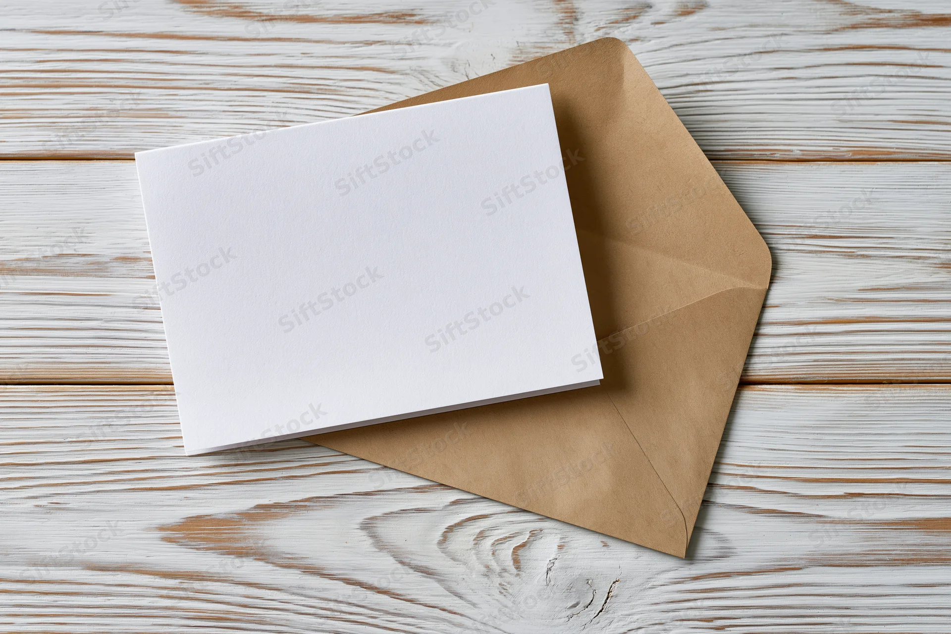 Blank white greeting card on kraft envelope resting on whitewashed wooden surface