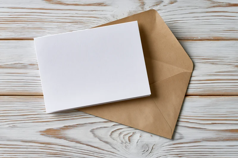 Blank white greeting card on kraft envelope resting on whitewashed wooden surface