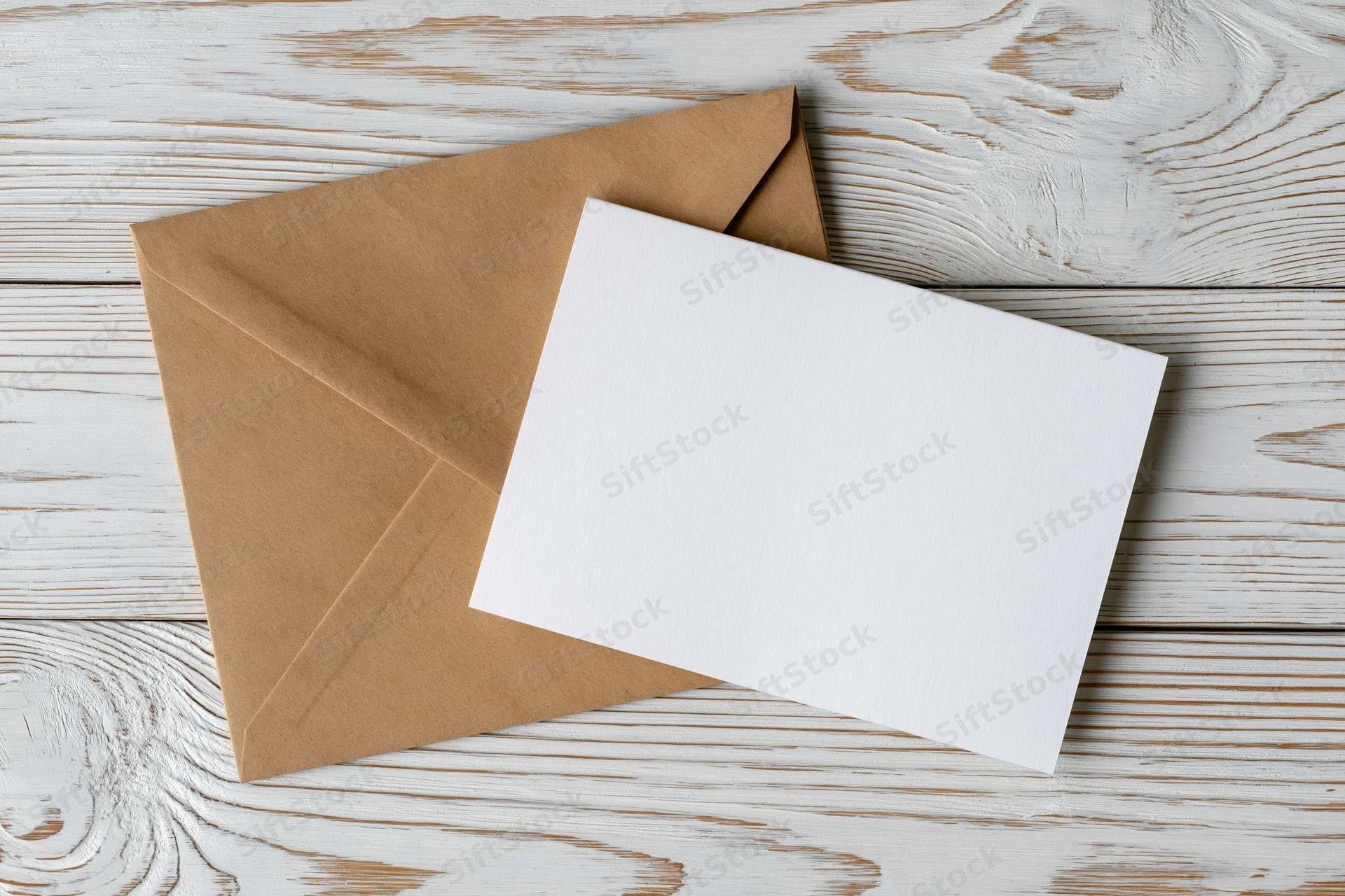 Blank white greeting card resting on a kraft paper envelope on a weathered white wooden surface