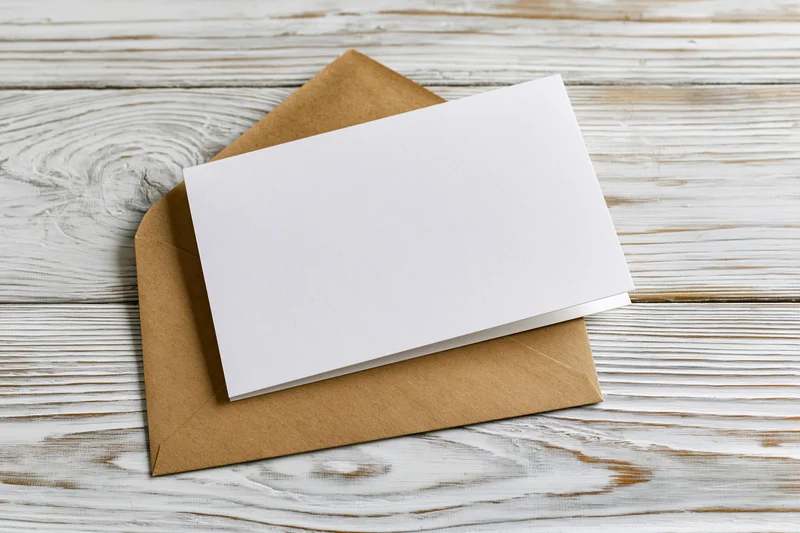 Blank white greeting card resting on a kraft paper envelope on a weathered wooden surface