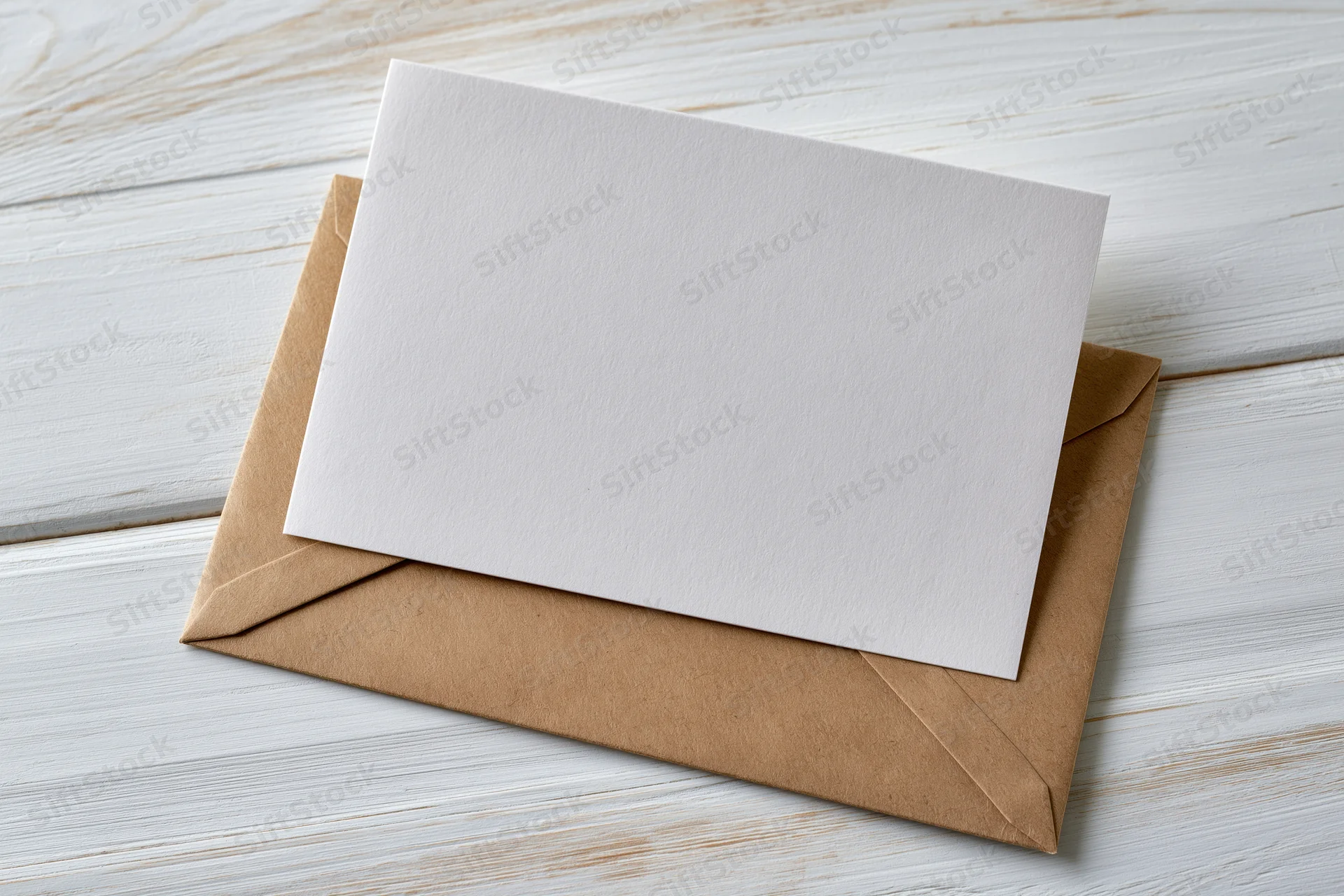Blank white greeting card resting on kraft envelope on whitewashed wooden surface