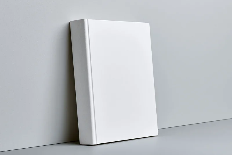 Blank white hardcover book leaning against a light gray wall in a studio setting