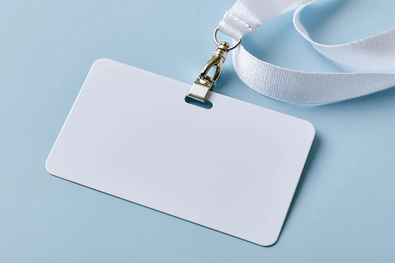 Blank white plastic badge card attached to white fabric lanyard on light blue surface