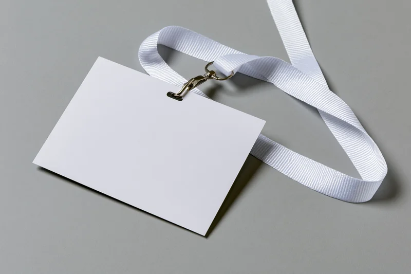 Blank white ID badge attached to white woven lanyard on gray surface