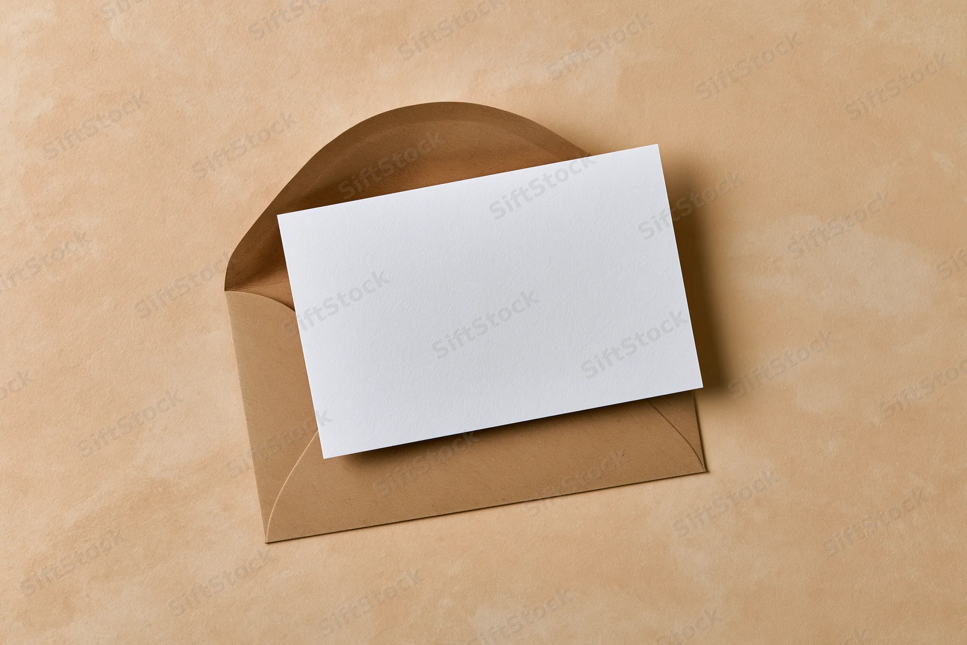 Blank white card resting on open kraft envelope on textured beige surface