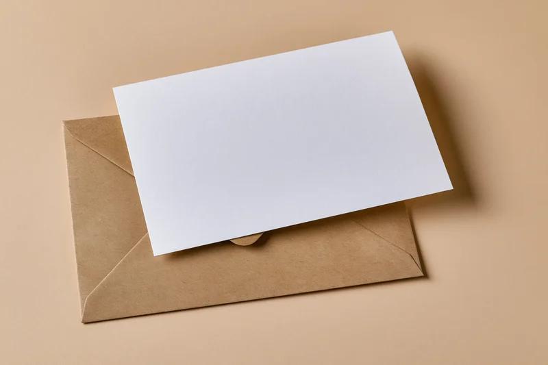Blank white card resting on a kraft paper envelope on a beige surface