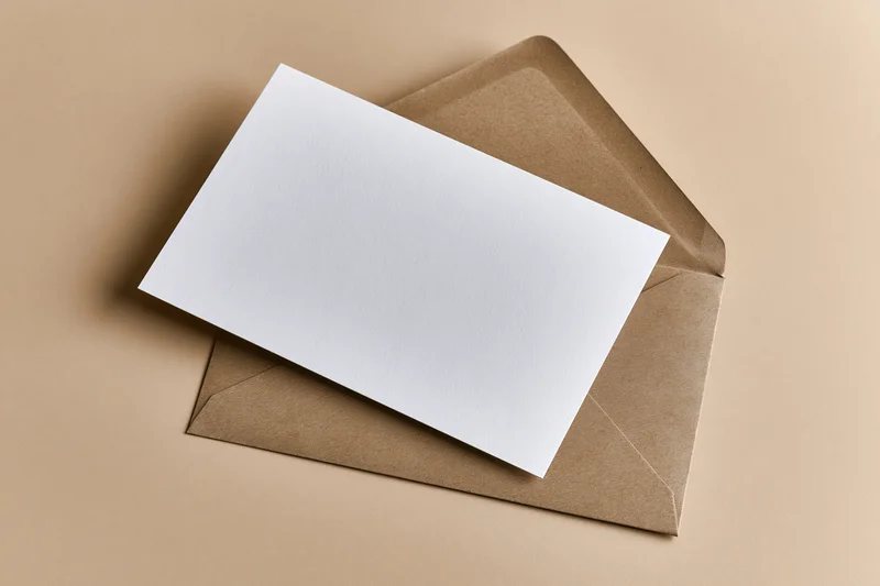 Blank white card resting on open kraft envelope on beige surface
