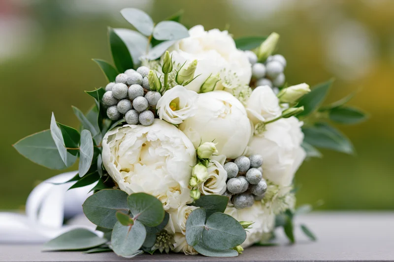 Bridal bouquet of white peonies and lisianthus with eucalyptus and silver berries on a table