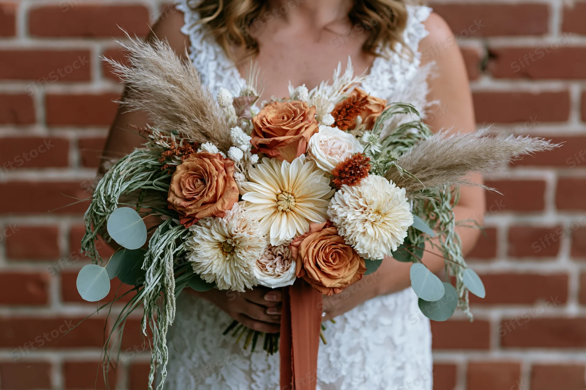 Bride holding cascading bouquet of orange and white flowers against brick wall
