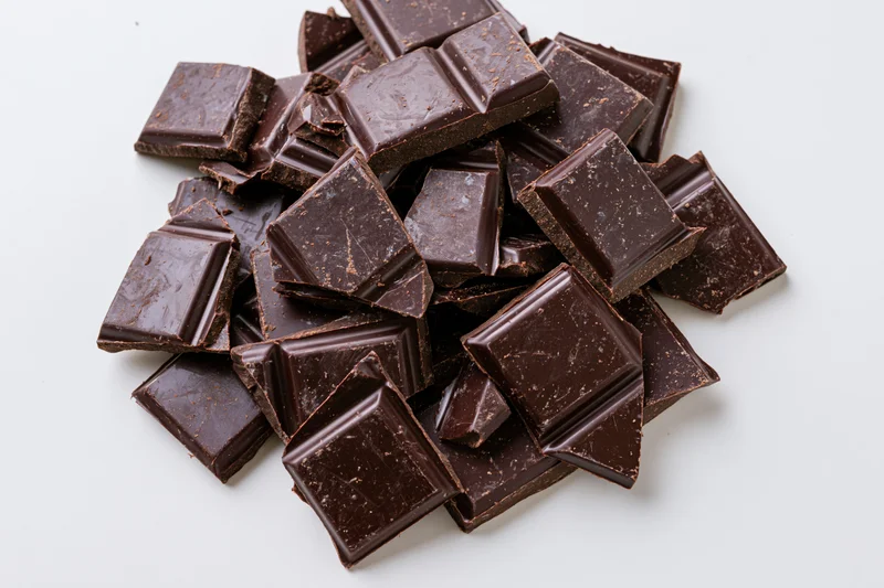Broken dark chocolate pieces scattered overhead on white background