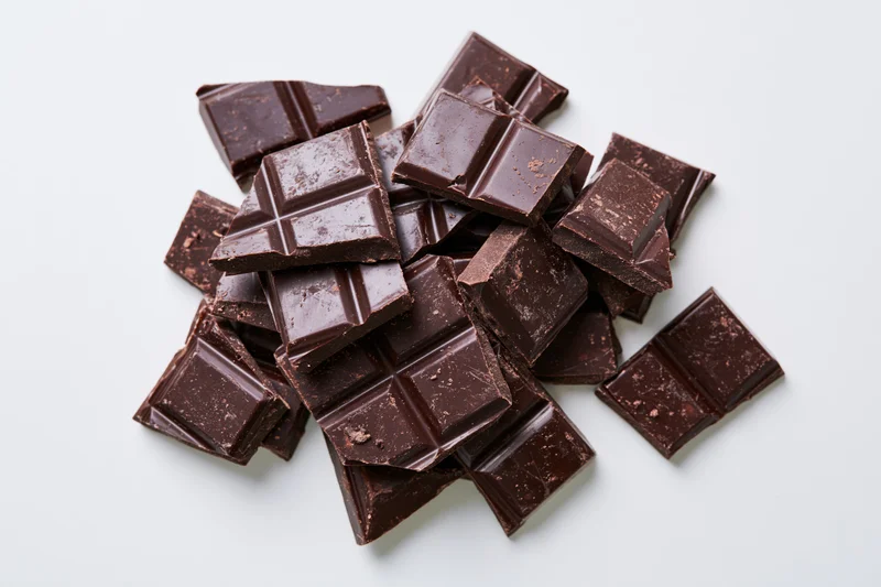 Broken dark chocolate bar pieces scattered overhead on white background