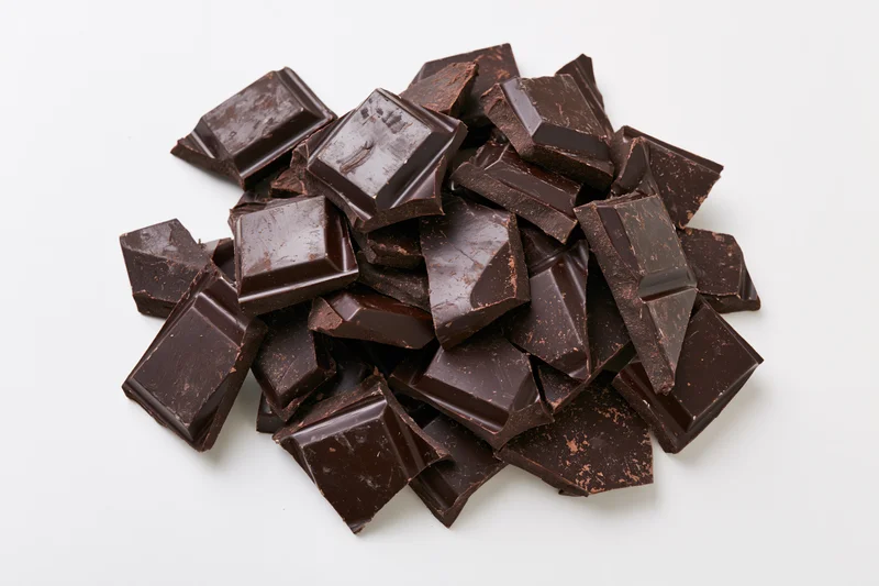Broken dark chocolate pieces scattered in a pile on white background