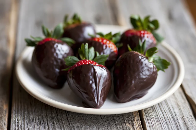 Chocolate-dipped strawberries arranged on a white ceramic plate on a wooden table