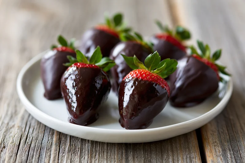Chocolate-dipped strawberries arranged on a white plate on a wooden table