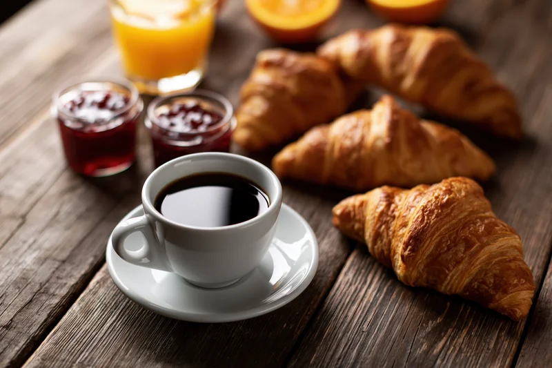 Croissants and coffee with orange juice and jam on a dark wooden table