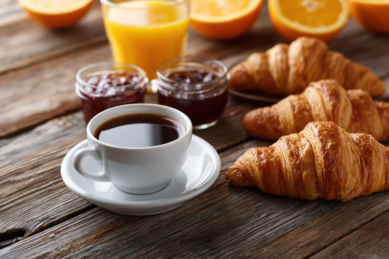 Croissants and coffee with orange juice and jam on a dark wooden table