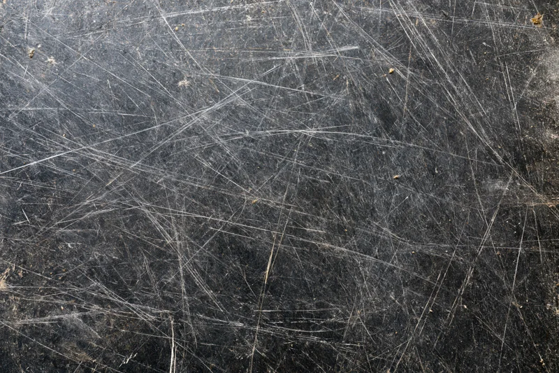Close-up of a heavily scratched dark metal surface showing wear and tear