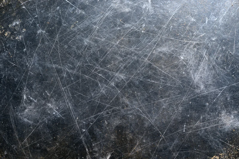 Close-up of heavily scratched dark metal surface with visible wear and texture
