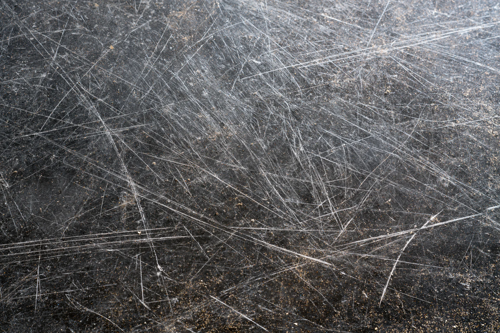 Close-up of a heavily scratched dark metal surface showing wear and industrial use