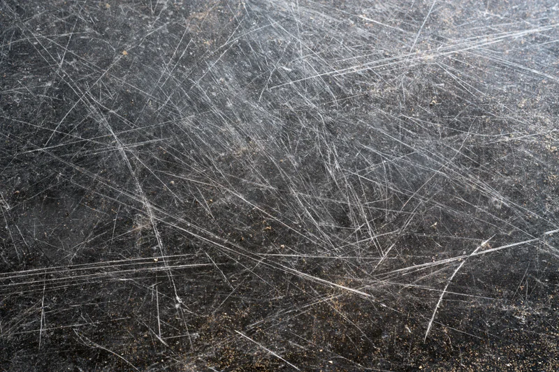 Close-up of a heavily scratched dark metal surface showing wear and industrial use
