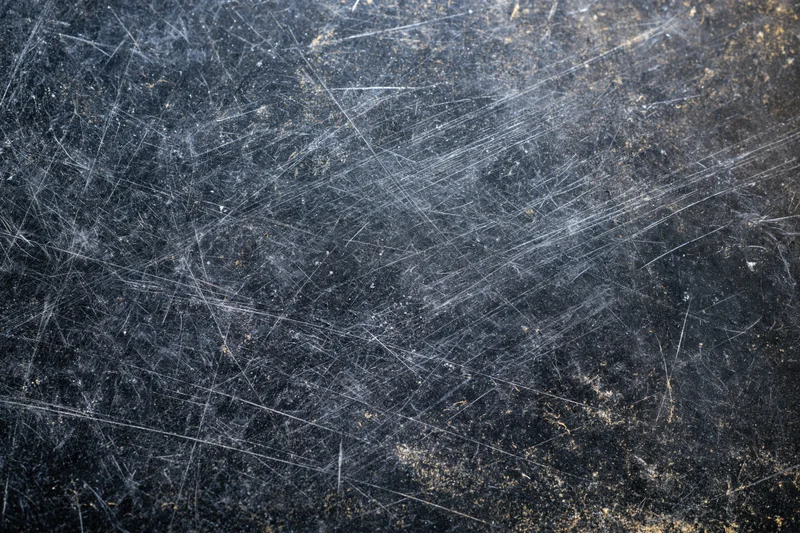 Close-up of a heavily scratched dark metal surface with visible wear and texture
