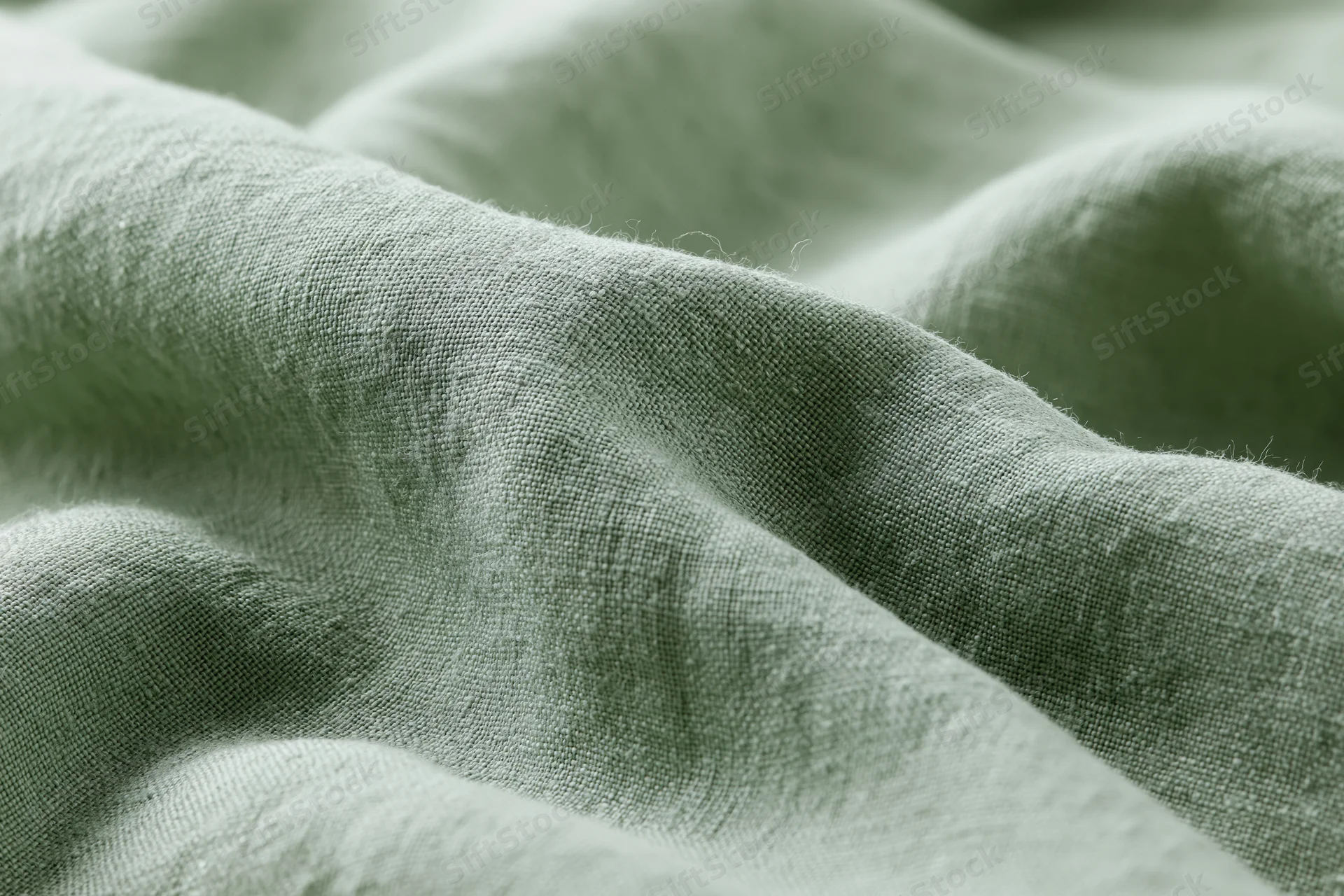 Close-up of sage green linen fabric with soft folds and natural texture filling the frame