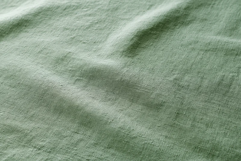 Close-up of sage green linen fabric with natural weave texture filling the frame