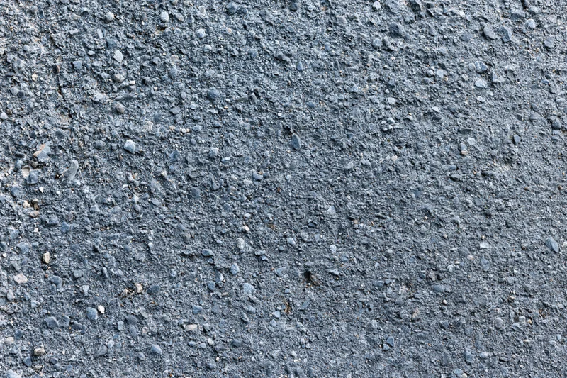 Close-up of rough asphalt road surface with embedded stones and cracks