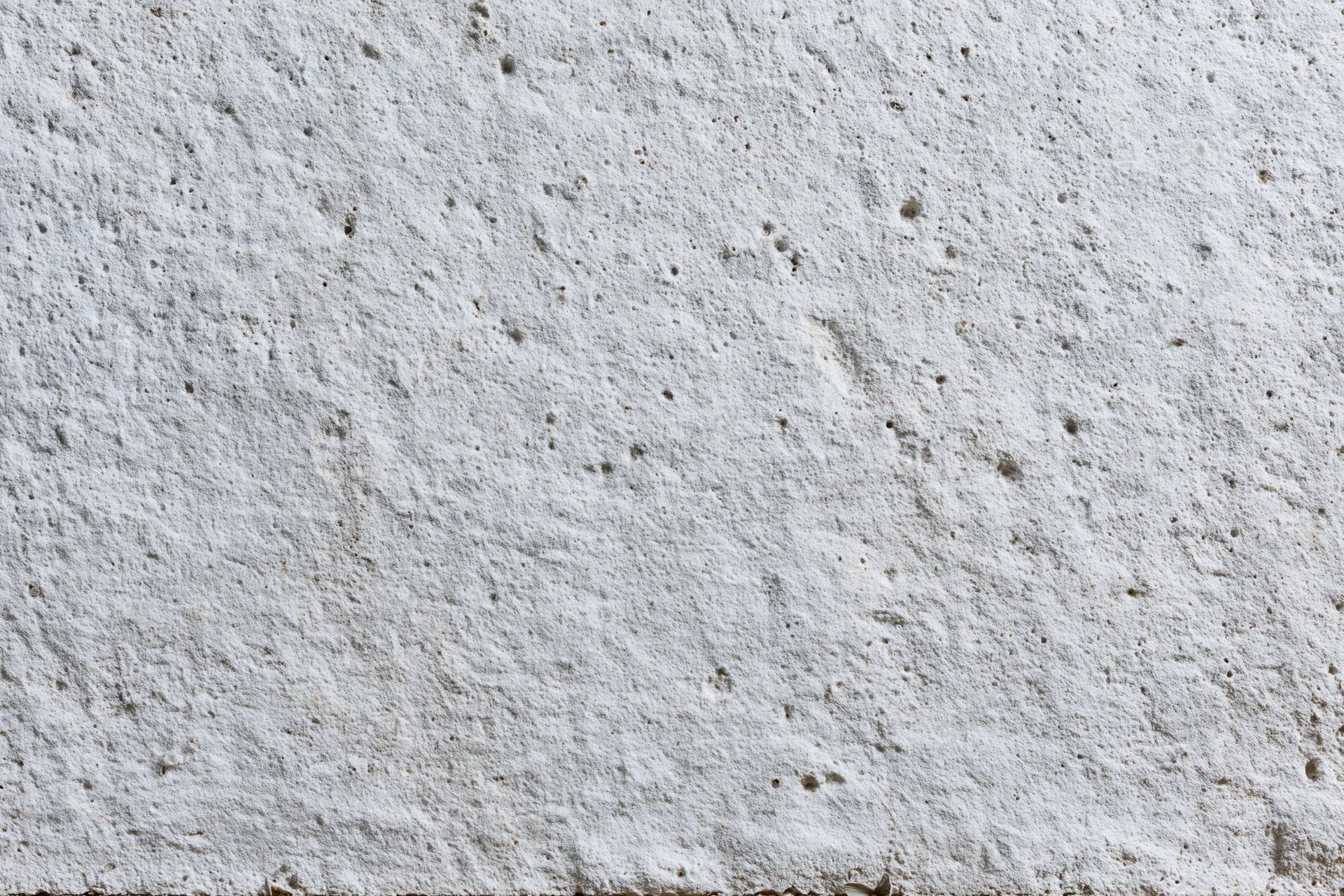 Close-up of a rough gray concrete wall surface with small pits and texture filling the frame