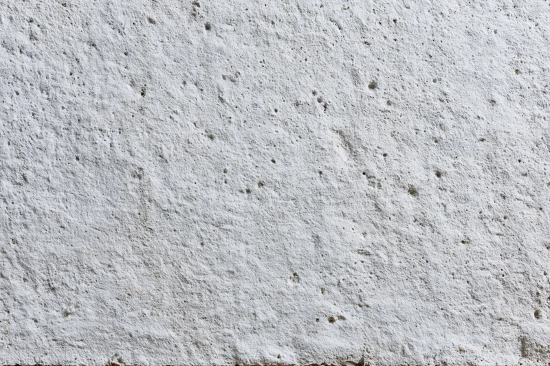 Close-up of a rough gray concrete wall surface with small pits and texture filling the frame